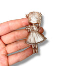 Gold figurine of a girl held in a hand against a white background.