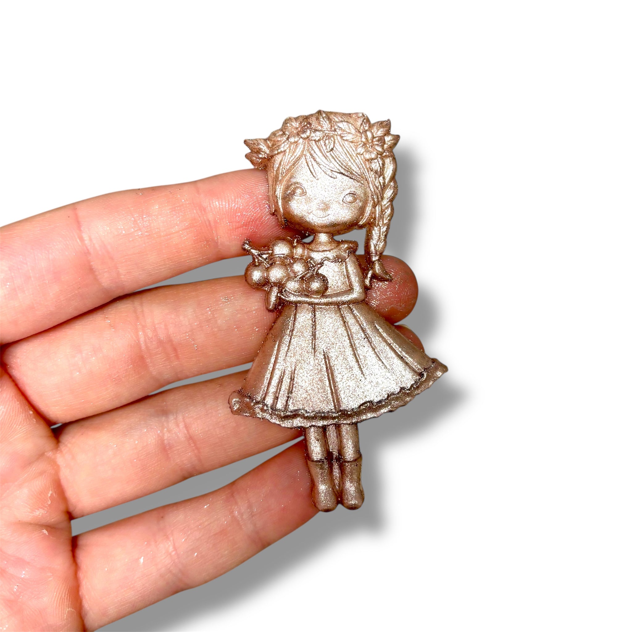Metallic figurine of a girl held in a hand against a white background