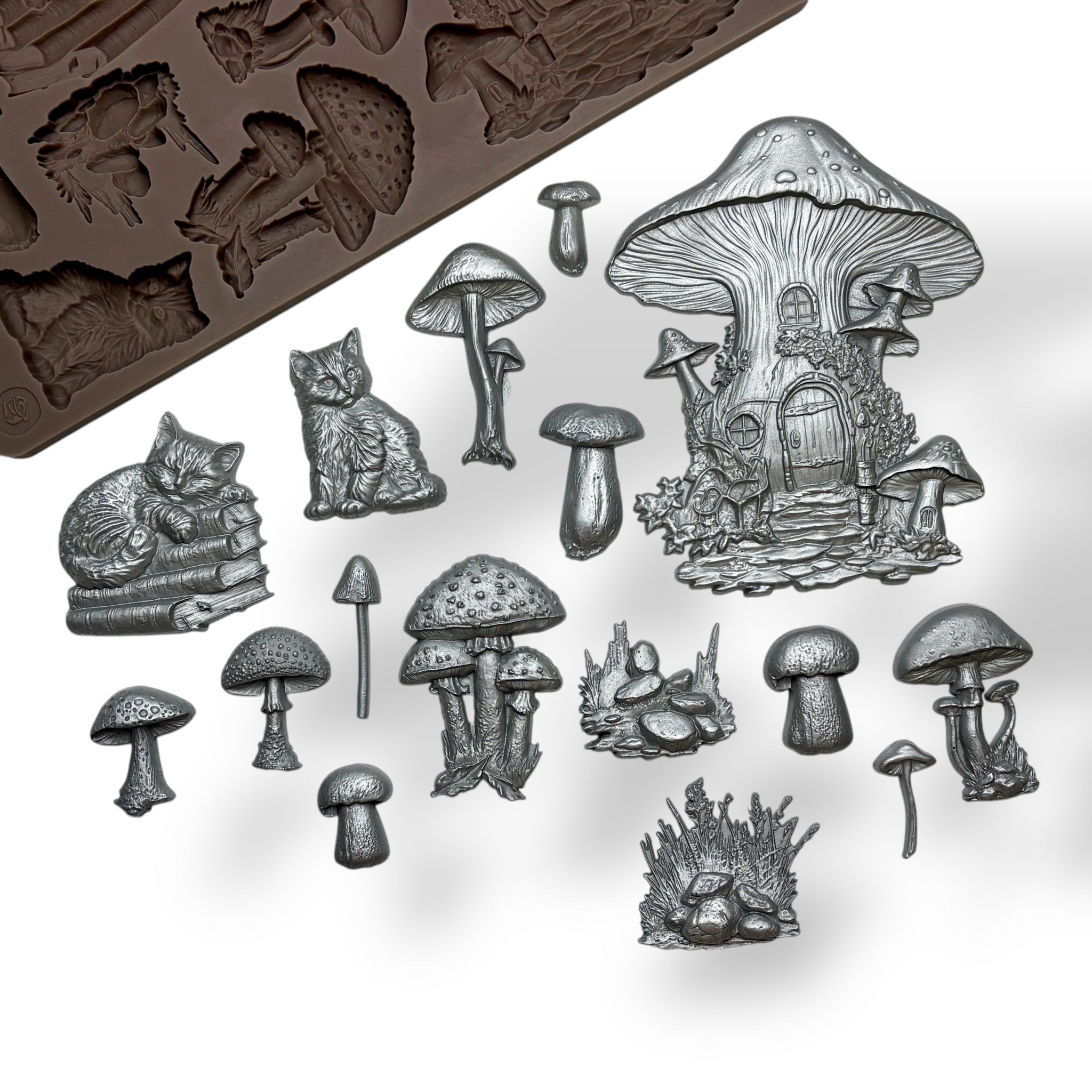 A brown silicone mold and silver colored castings of mushrooms, a fairy mushroom house, and cats are against a white background. 