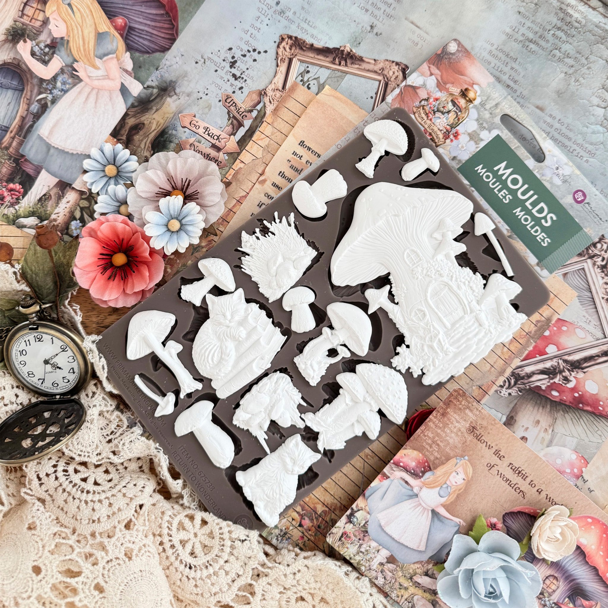 A package of Prima Marketing's Fairyland Fungi silicone mold and white castings laying on the mold are on a table with Alice in Wonderland scrapbook decor.