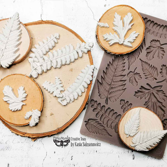 Leaf-shaped cookie cutters on wooden slices with a silicone mold featuring leaf patterns.