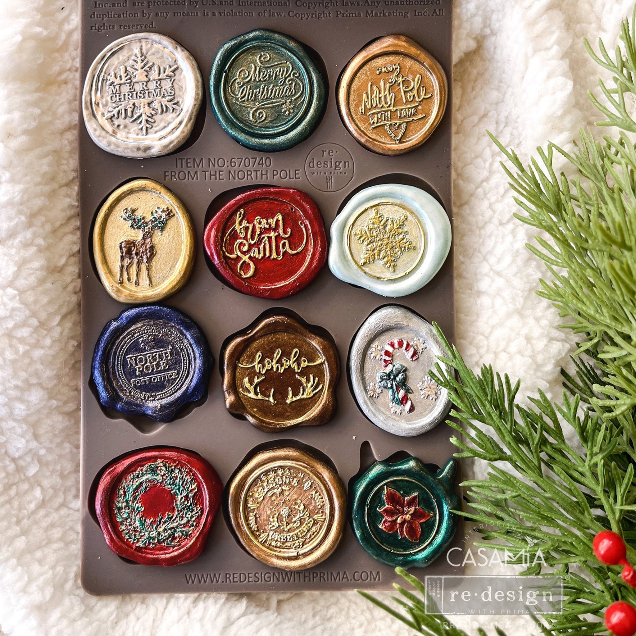 A brown silicone mold and colorful castings of 12 Christmas and holiday wax seals are against a white Sherpa blanket.