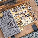 Set of metal letter and number stamps on a wooden surface with gears.
