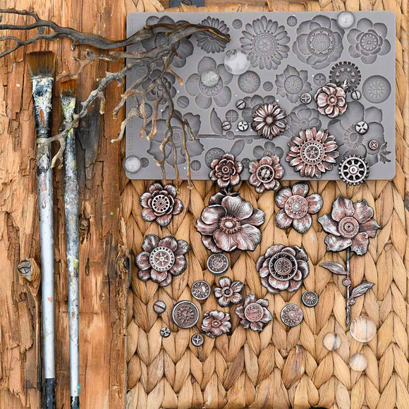 Decorative metal flowers on a textured surface with a paintbrush and branch.