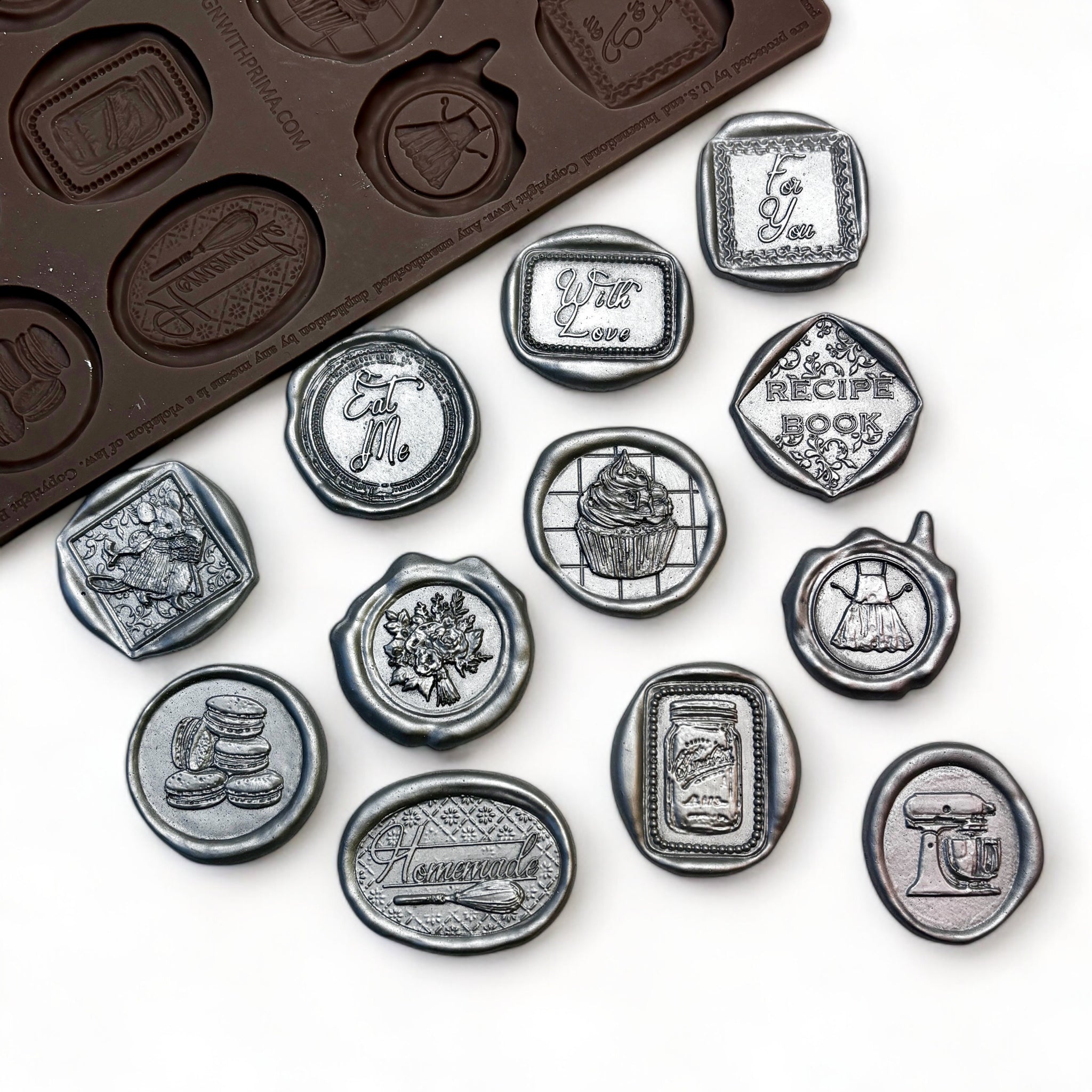 A brown silicone mold and silver colored castings of 12 baking themed wax seals are against a white background.