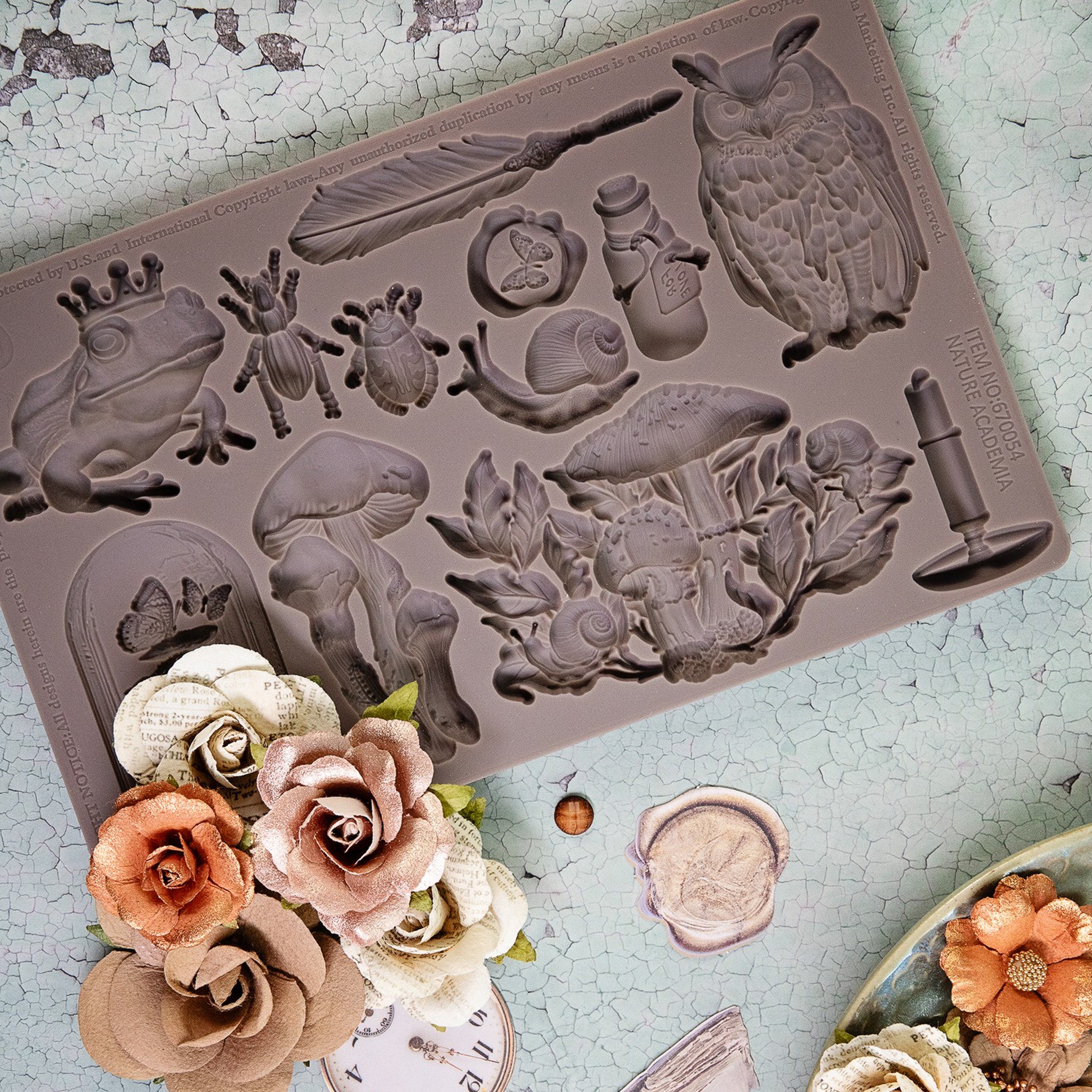 A brown silicone mold featuring bugs and mushrooms is against a crackle background. A bouquet of flowers sits at the bottom left of the mold.
