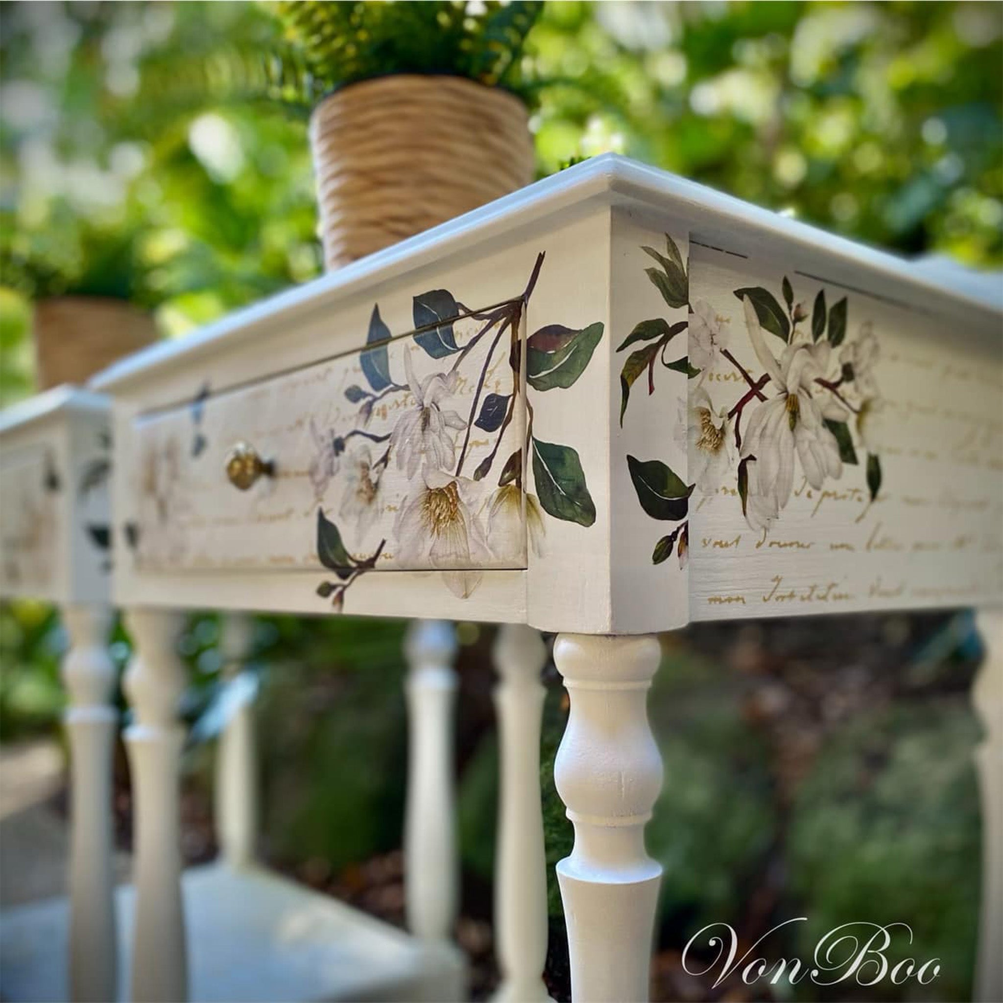 A close-up of 2 vintage side tables each with 1 small drawer refurbished by Von Boo are painted white and feature ReDesign with Prima's White Magnolia small transfer on them.