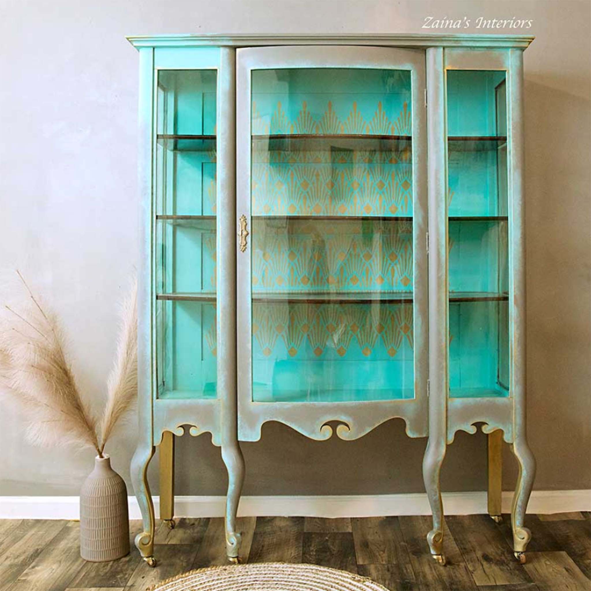 A wood and glass hutch refurbished by Zaina's Interiors is painted a blend of light aqua and beige on the outside wood and light aqua on the interior wood. ReDesign with Prima's Sunlit Diamonds stencil in gold is featured against the inside backboard.