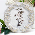 14" Paulownia Wood Charger is painted white with scrolling moulding on it and a transfer of flowers in the center.