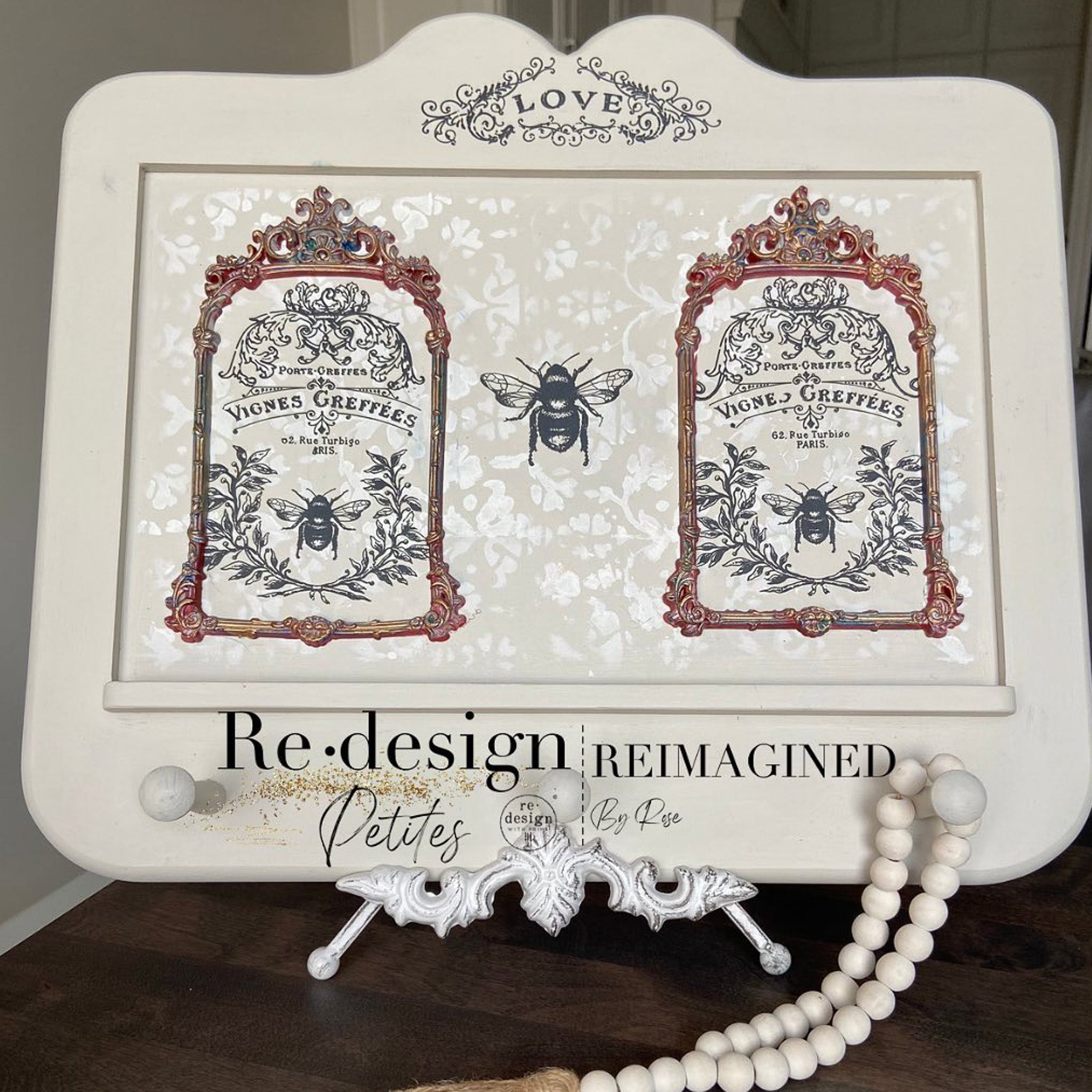 A wood craft project on a plate holder stand refurbished by Reimagined by Rose is painted cream and features ReDesign with Prima's French Labels on it.