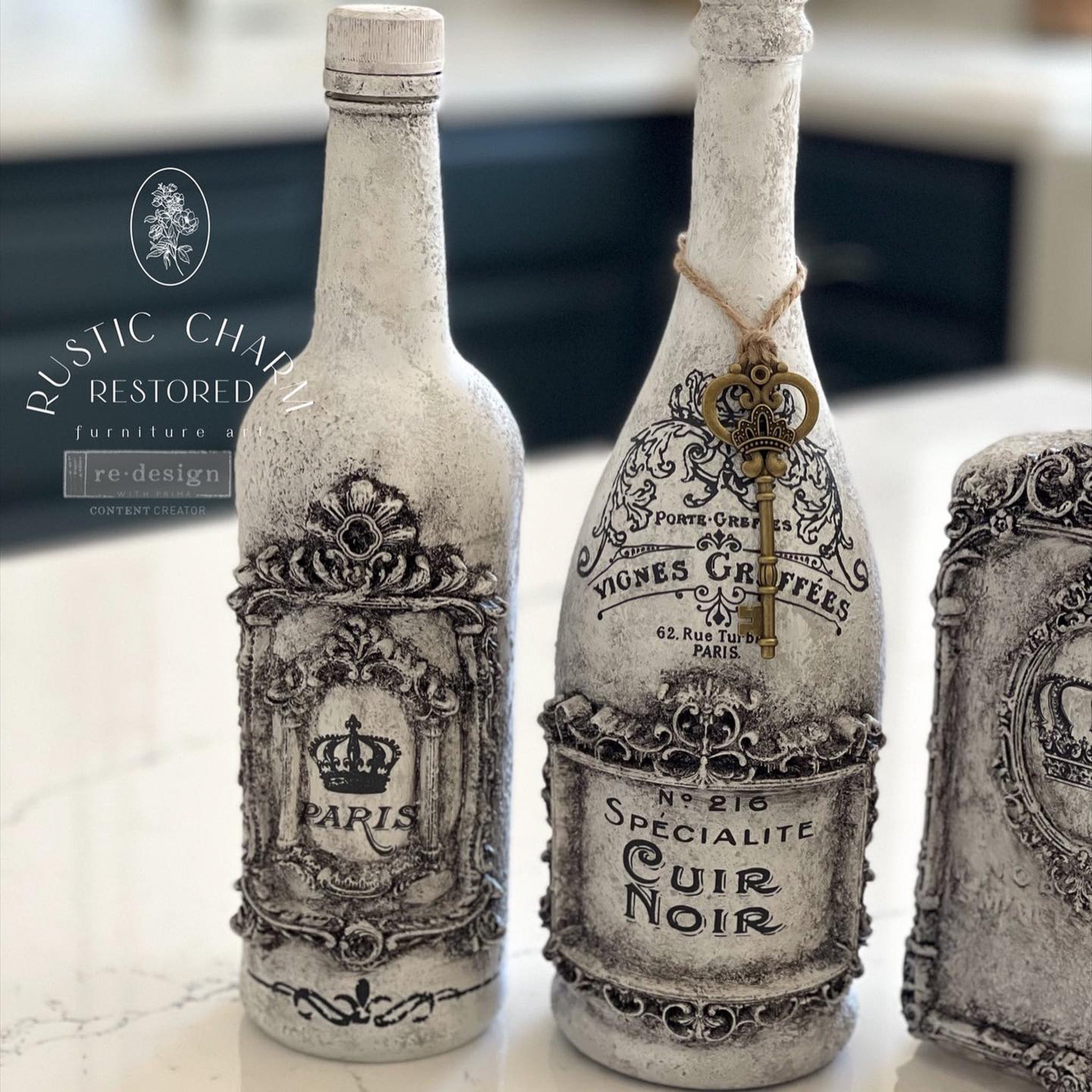 Two glass bottles refurbished by Rustic Charm Restored are painted white with black antiquing and features ReDesign with Prima's French Labels small transfer on them along with some silicone mould castings.