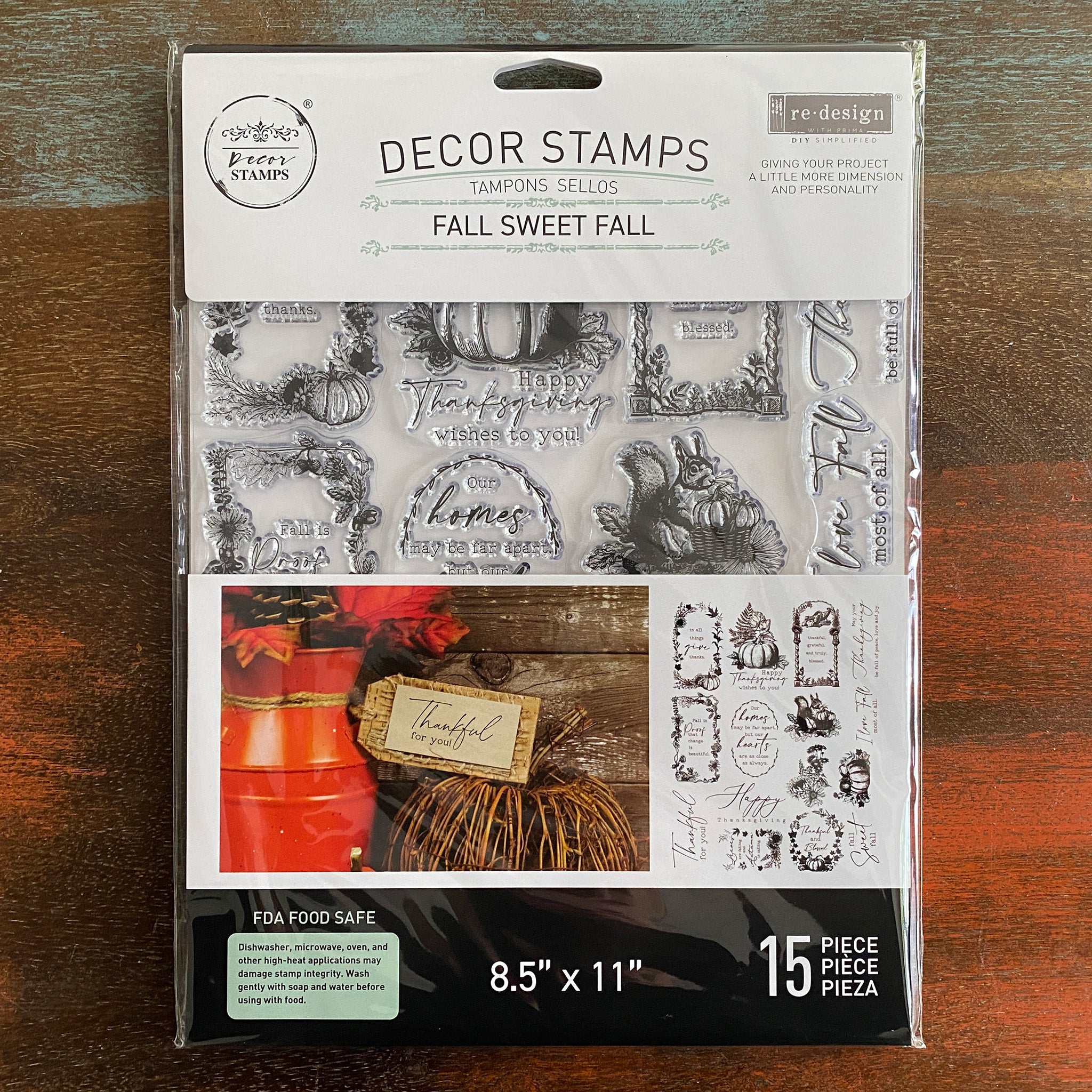 A package of ReDesign with Prima's Fall Sweet Fall Decor Stamps is against a dark wood background.