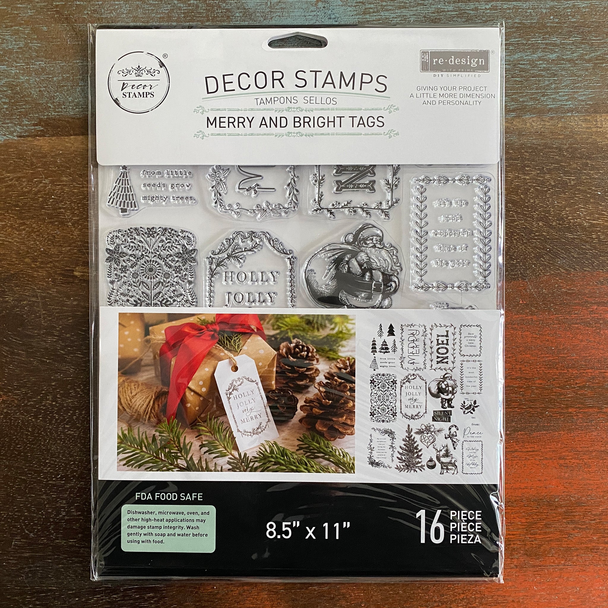 A package of ReDesign with Prima's Merry and Bright Decor Stamps is against a dark wood background.