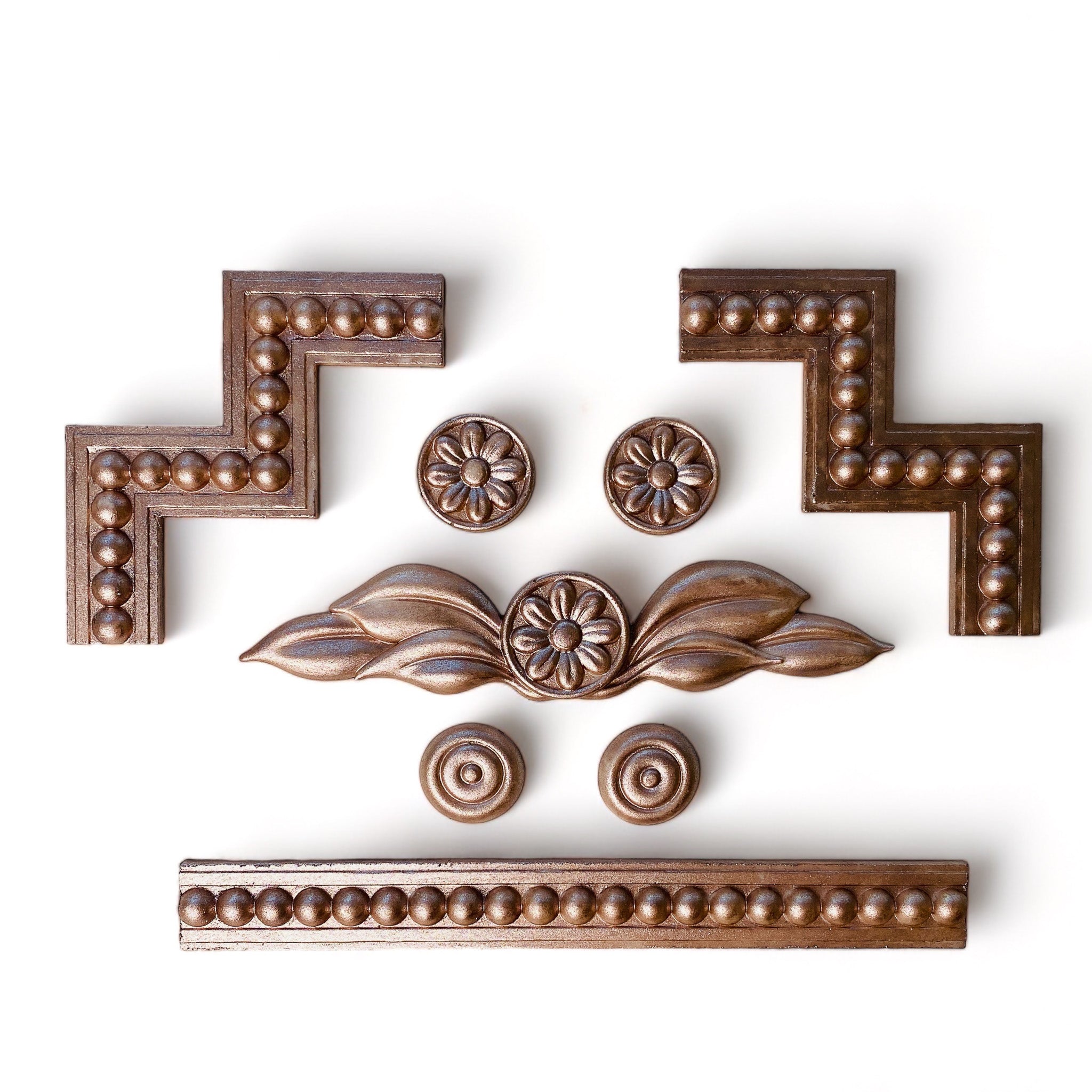 Copper colored silicone mold castings featuring unique edge pieces, borders, and multiple small floral medallions are against a white background.