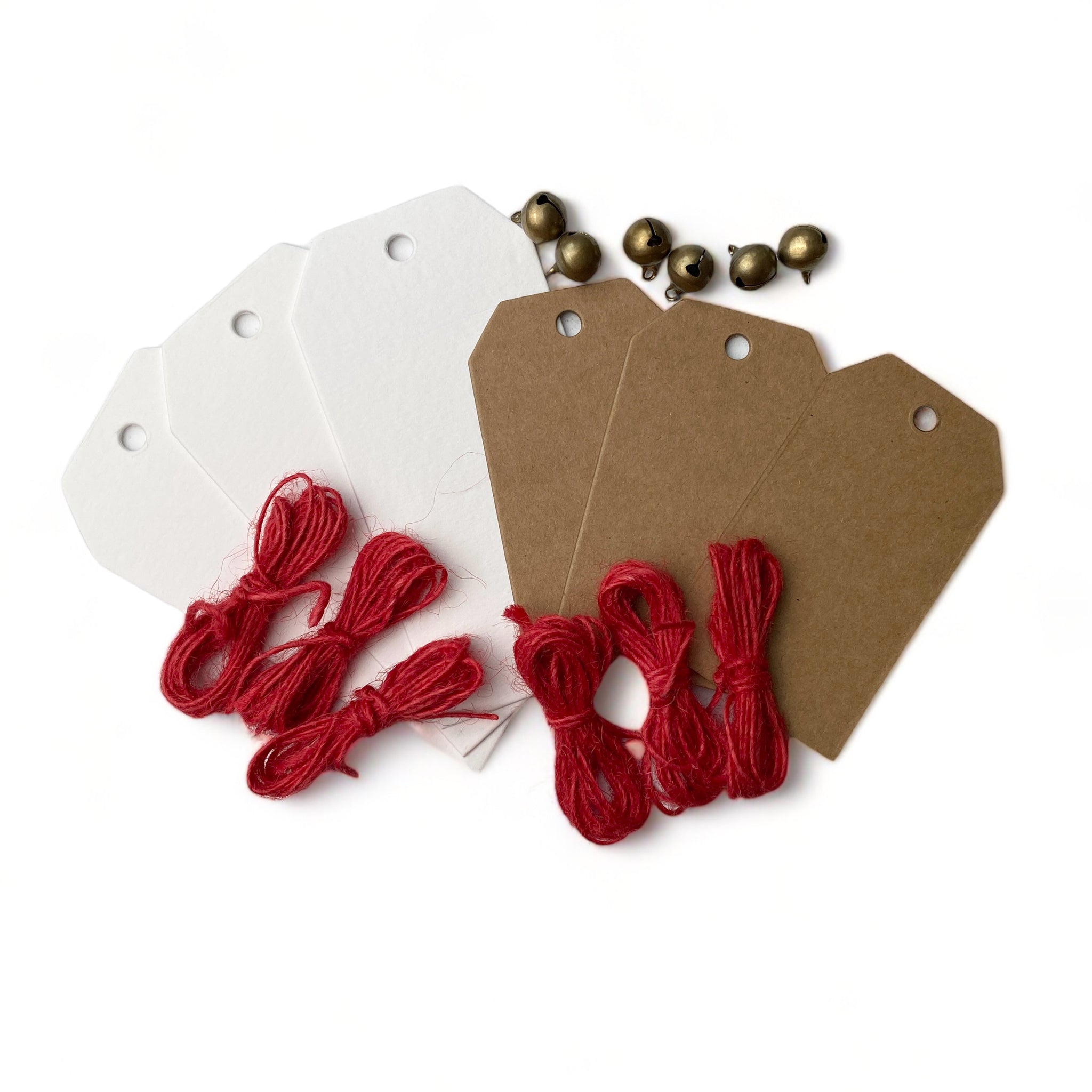 Three white and 3 brown chipboard Christmas gift tags, 6 small gold round bells, and red string are against a white background.