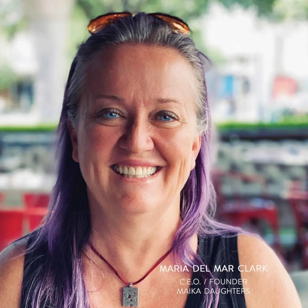 Maria Del Mar Clark, founder and CEO of Maika Daughters, smiling with purple hair and pendant necklace—creative entrepreneur behind upcycling and DIY furniture supplies.