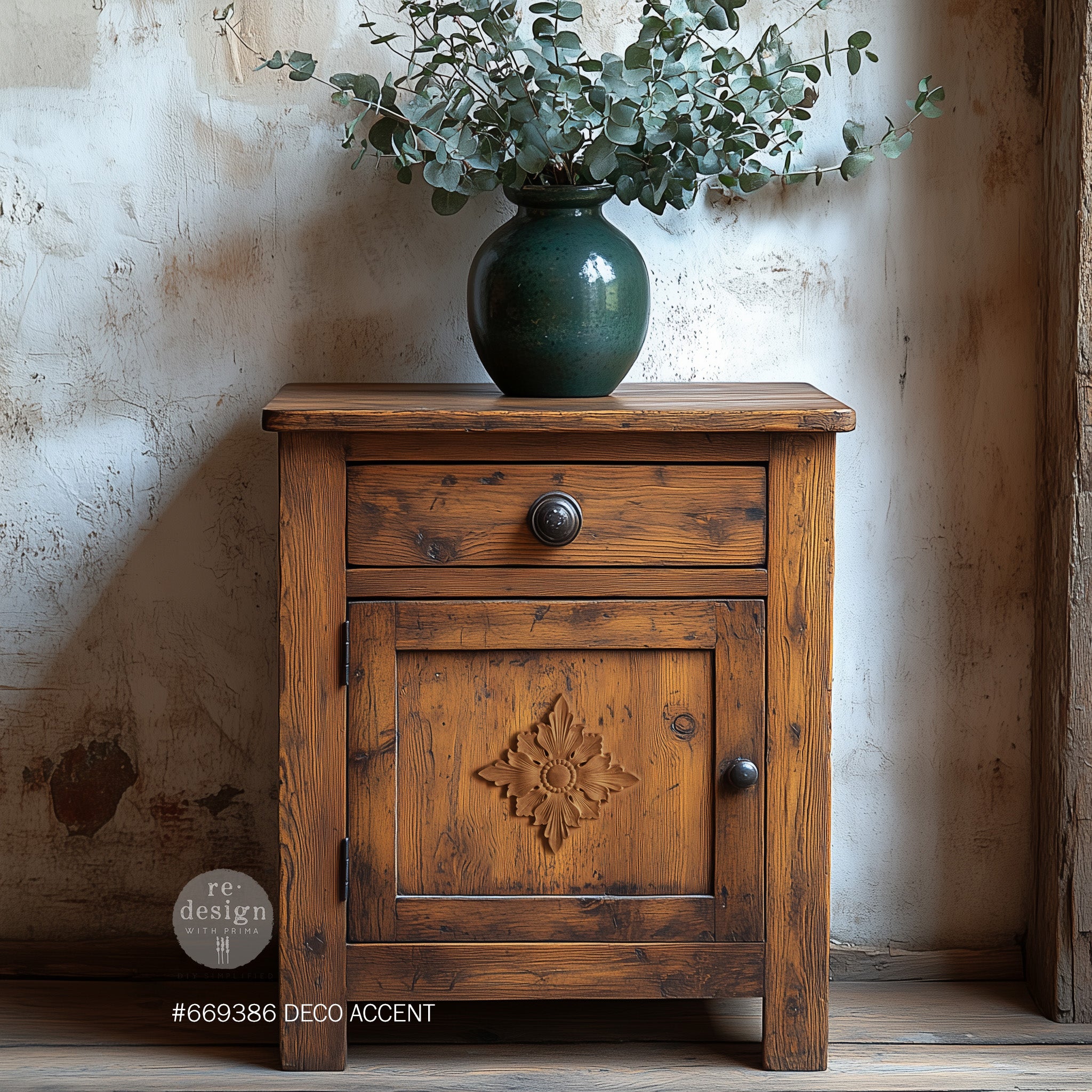 A vintage nightstand with storage is stained natural wood and features ReDesign with Prima's Deco Accent Decor Poly furniture applique in the center of its door under a drawer and is painted a color to match the wood.