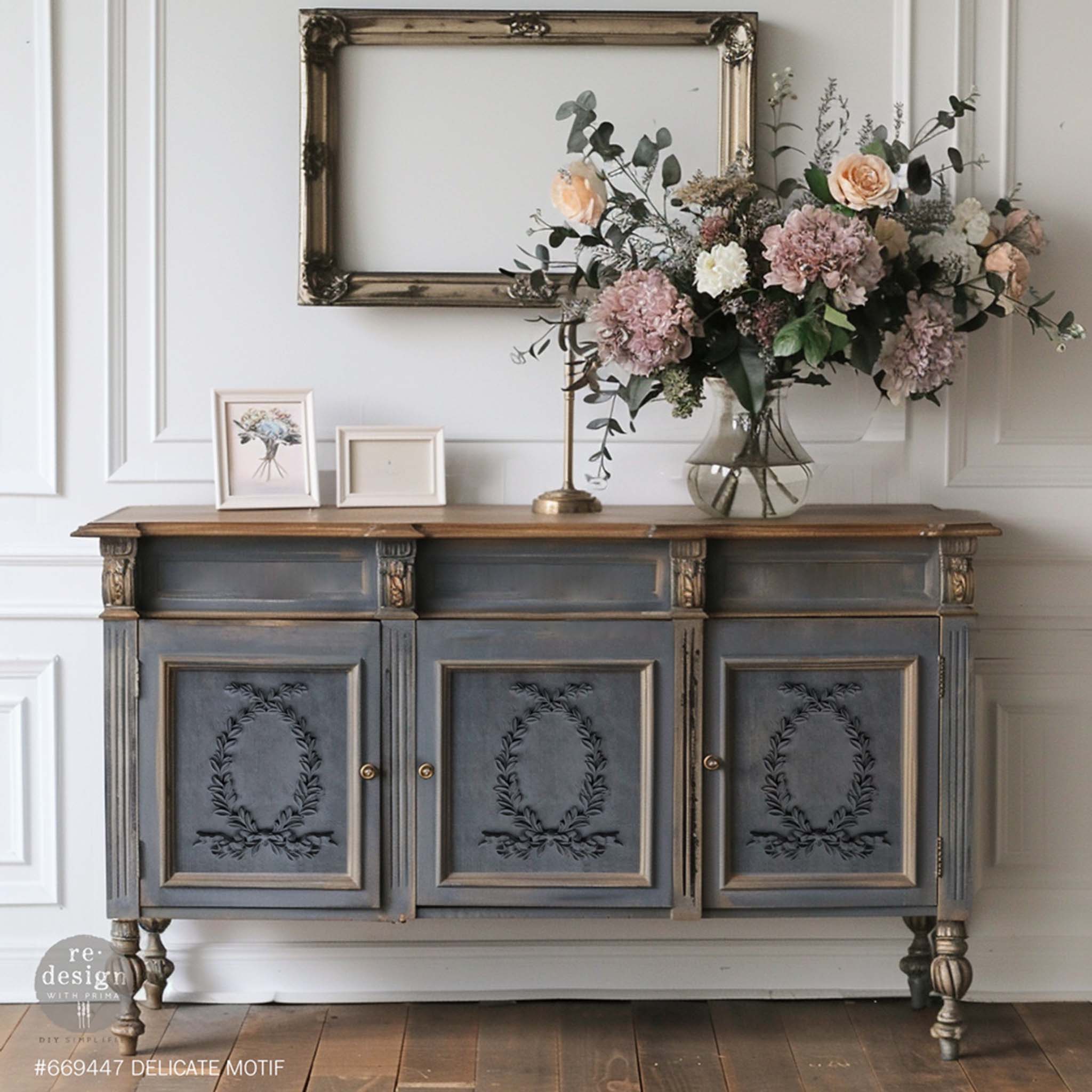 A vintage console table with is painted gray with bronze accents and features ReDesign with Prima's Delicate Motif Decor Poly Casting bendable furniture appliques on its 3 doors.