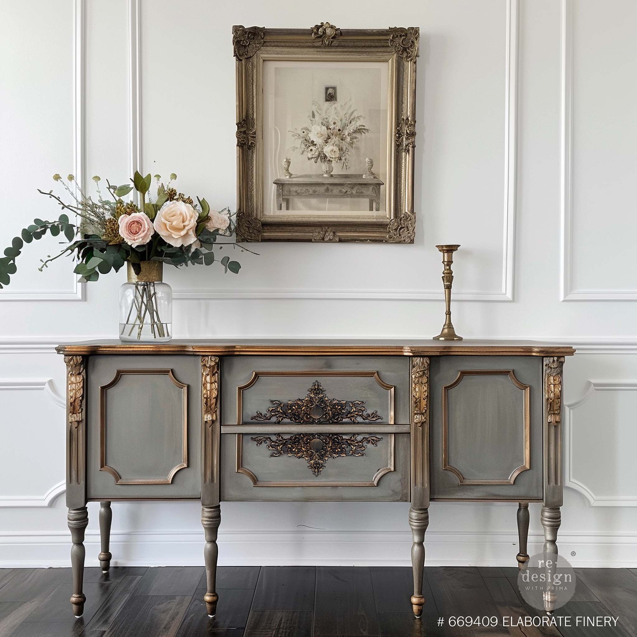 A vintage console table is painted gray with bronze accents and features ReDesign with Prima's Elaborate Finery Decor Poly Casting on 2 center drawers.