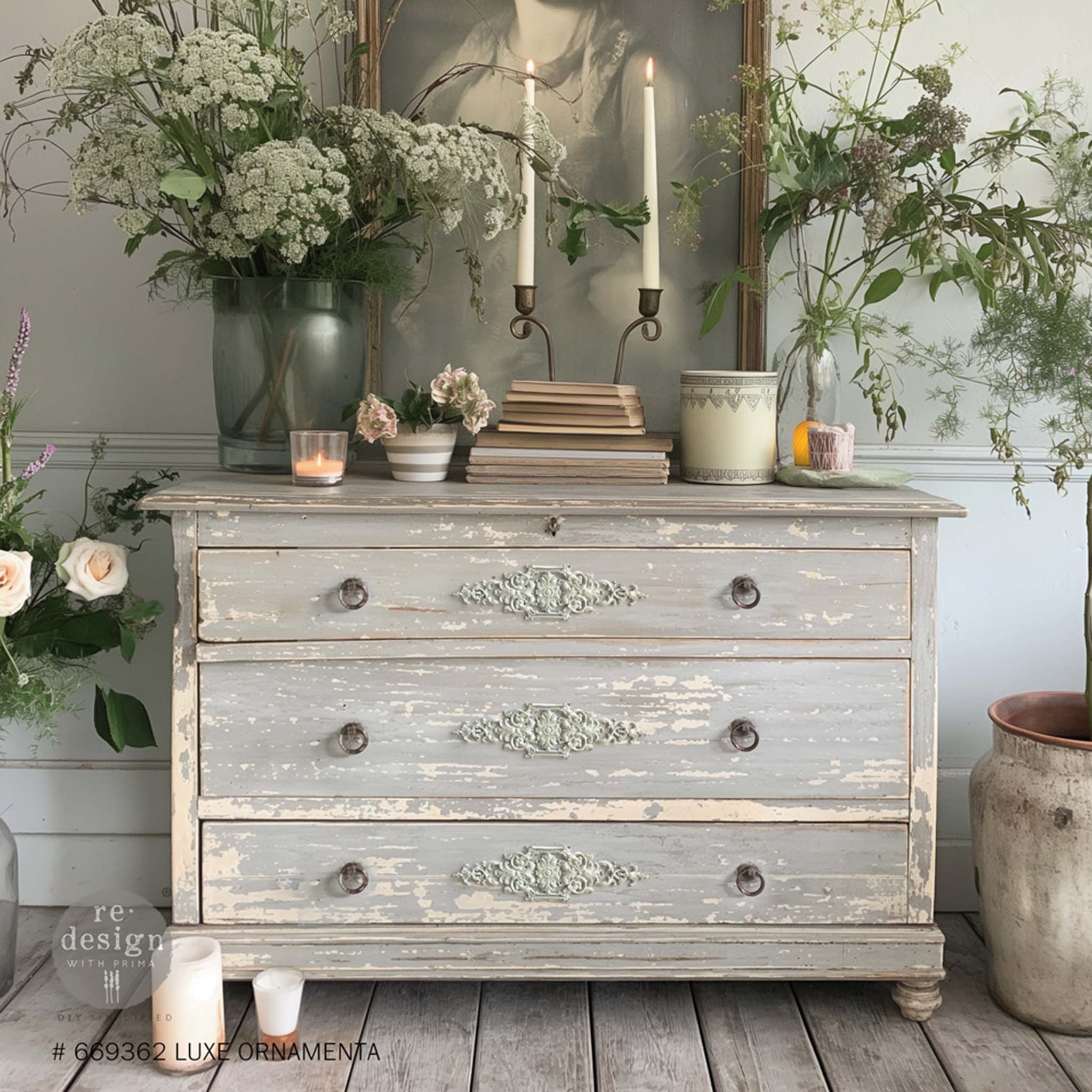 A vintage 3-drawer dresser is painted a weathered light gray and features ReDesign with Prima's Luxe Ornamenta Decor Poly Casting in the center of each drawer.