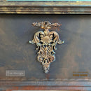 A close-up of ReDesign with Prima's Regal Finasse Decor Poly Casting painted in gold by Ilse Lievegoed is shown against a mottled gray piece of furniture.