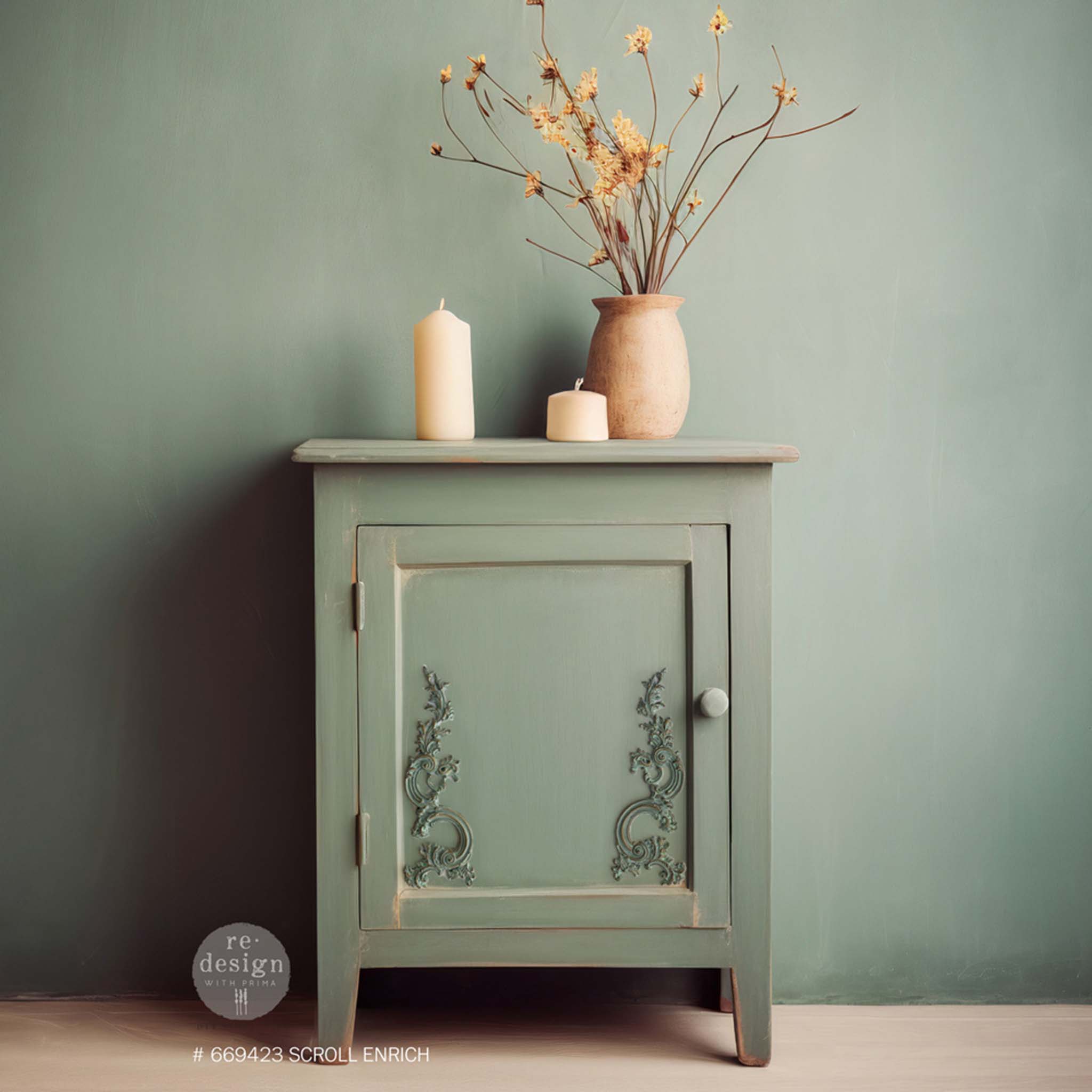 A small side table with storage is painted light sage green and features ReDesign with Prima's Scroll Enrich Decor Poly Casting on the bottom right and left inlay door corners.