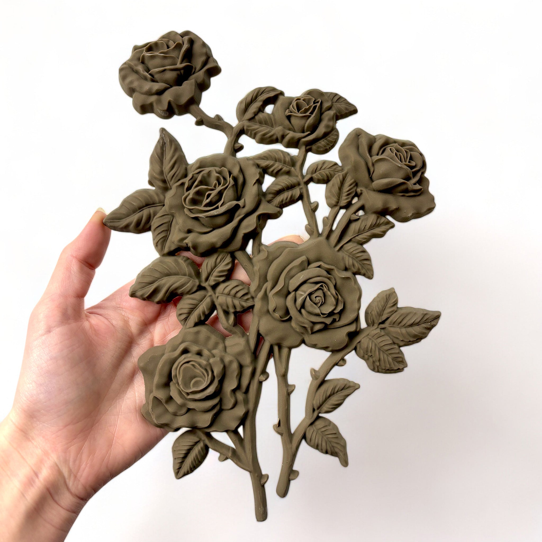 A hand is shown holding a brown colored bendable furniture applique of a small bouquet of 6 roses against a white background.