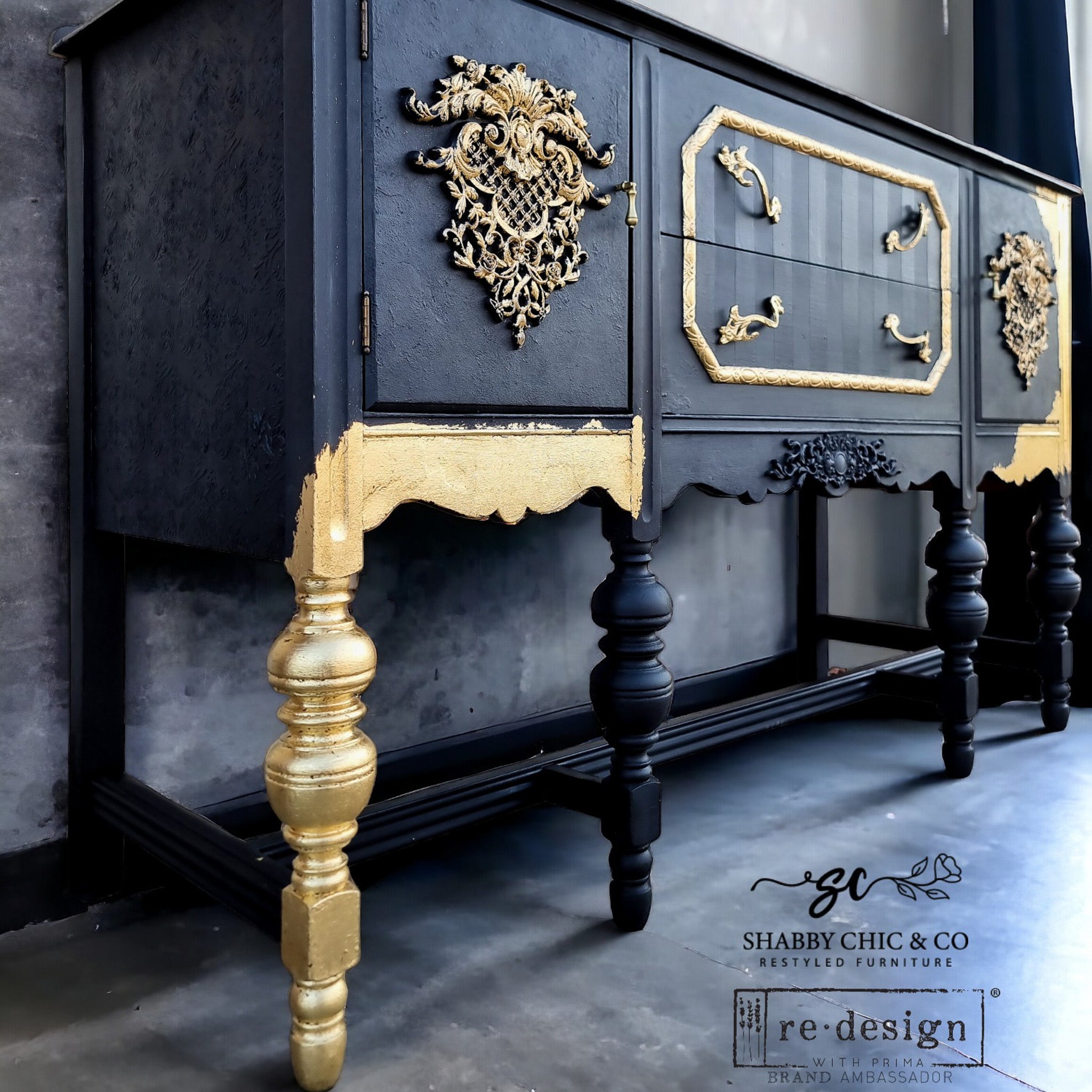 A vintage console table refurbished by Shabby Chic & Company is painted black with gold accents and features ReDesign with Prima's Baroque Elegance Decor Poly painted gold on its 2 doors.