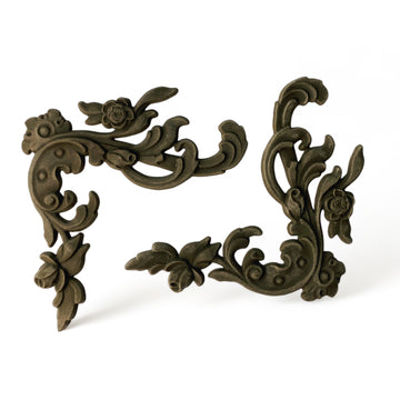 Two bendable furniture appliques that feature corner flourishes, adorned with delicate leaves and flowers are against a white background.