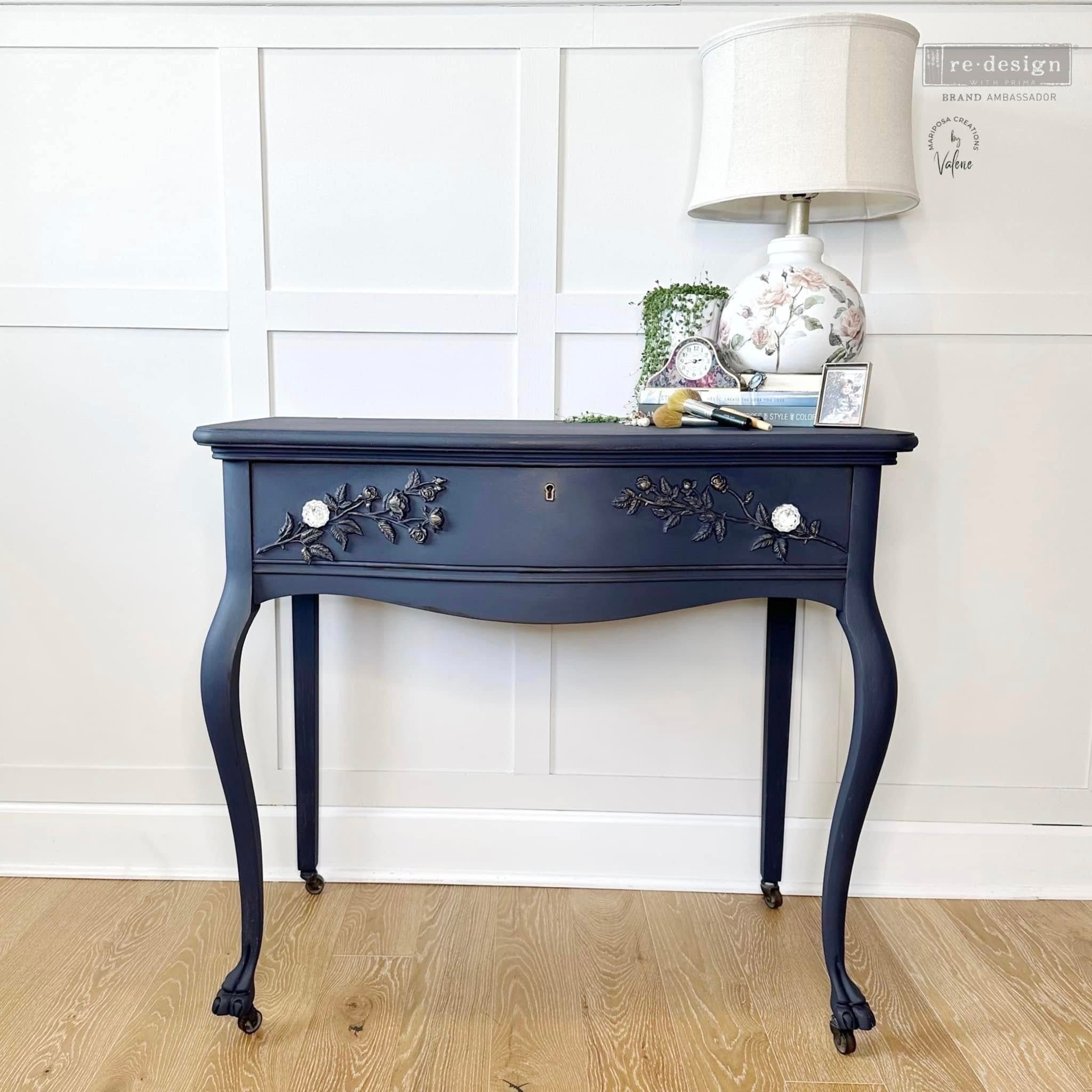 A vintage console table with 1 drawer is painted navy blue and features ReDesign with Prima's Petals in Harmony Decor Poly painted in navy blue on the drawer.