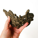 A hand is shown flexing a bendable furniture applique that features intricate flourishes, a lattice center, and floral accents against a white background.