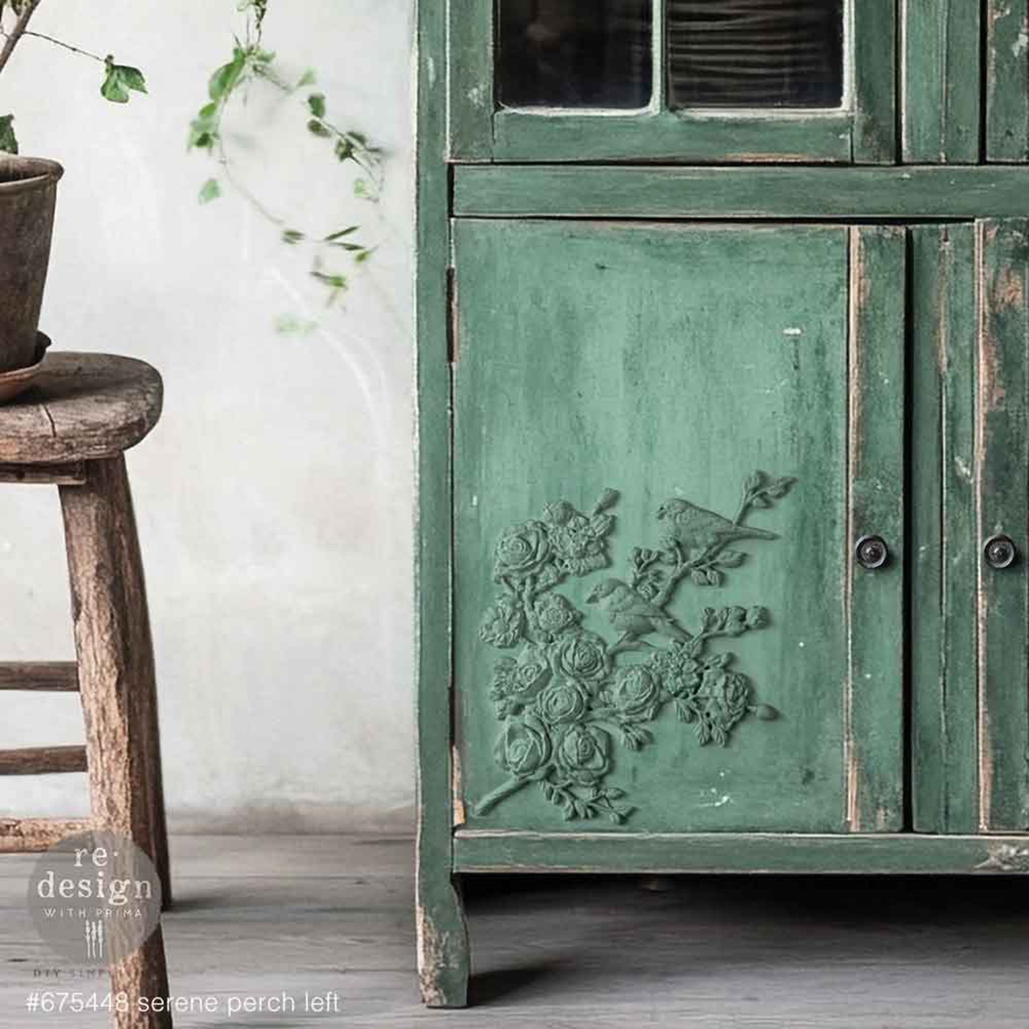 A close-up of a vintage country hutch cabinet is painted green and features ReDesign with Prima's Serene Perch (Left) on its left cabinet door.