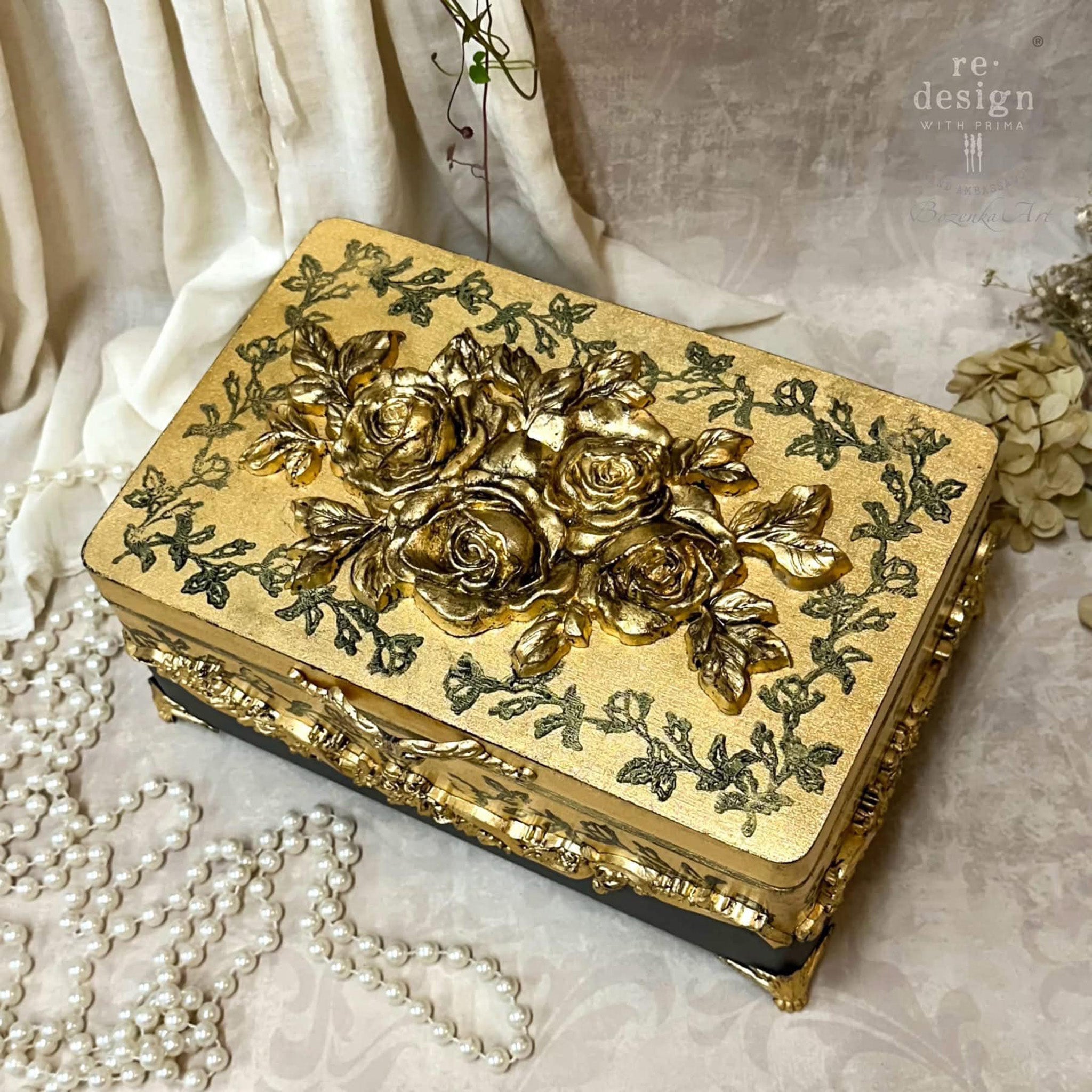 A small gold painted jewelry box features ReDesign with Prima's Timeless Petals Decor Poly painted in gold on its lid.