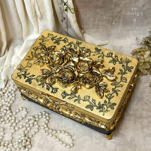 A small gold painted jewelry box features ReDesign with Prima's Timeless Petals Decor Poly painted in gold on its lid.