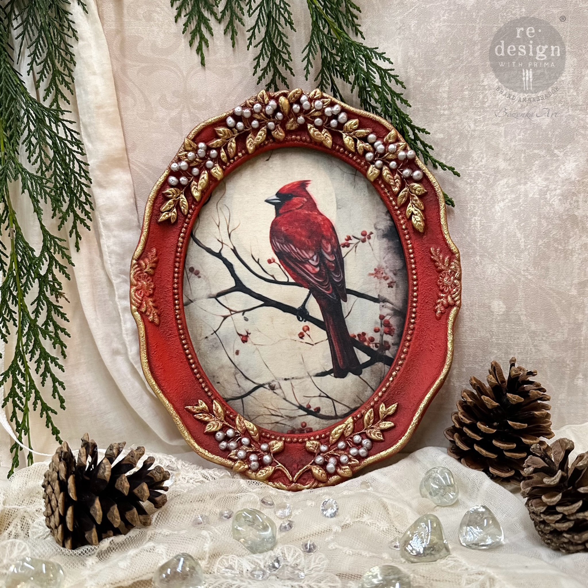 An oval frame painted red with gold and silver colored berry accents features a design from ReDesign with Prima's Festival Cardinal A3 fiber paper in it.