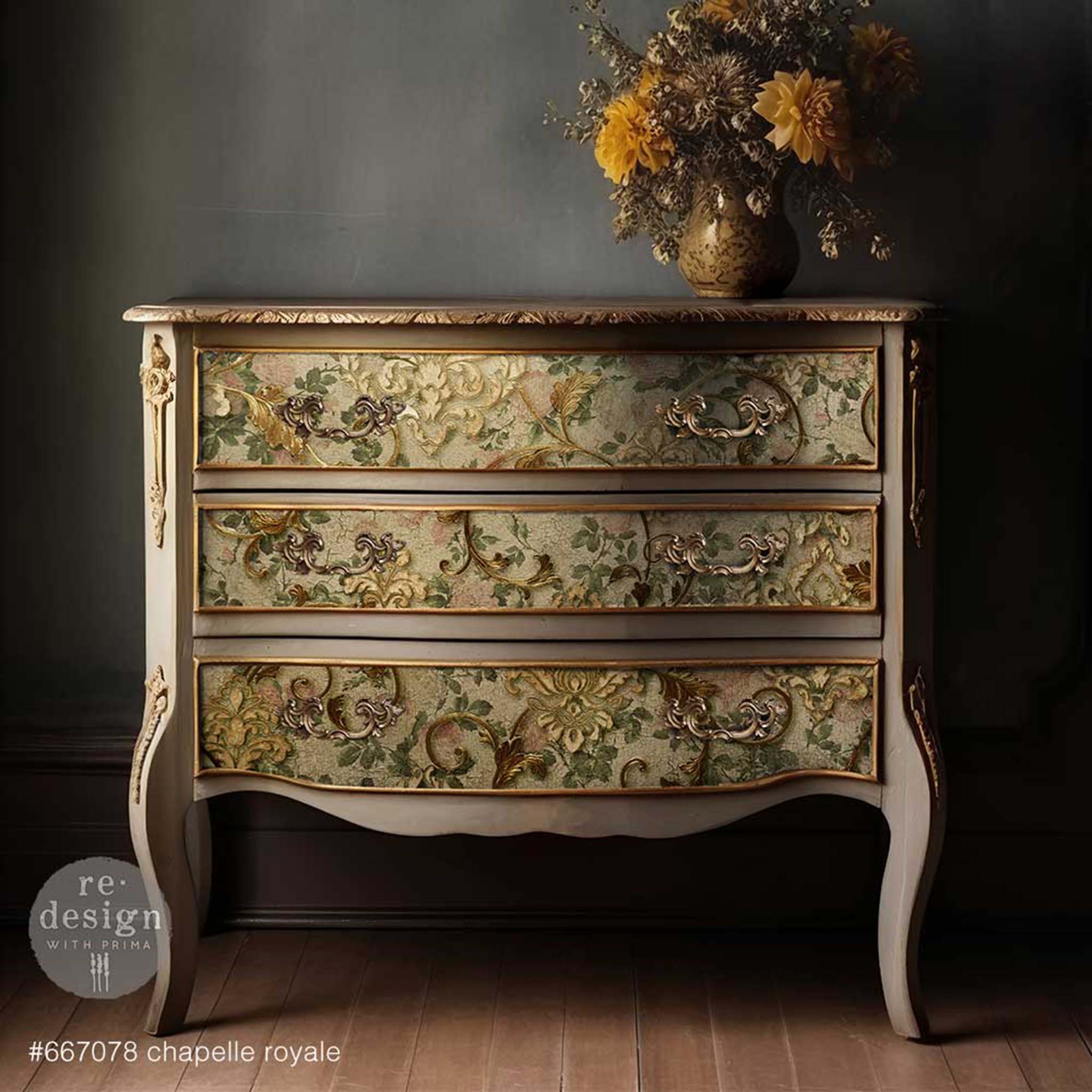 A vintage 3-drawer dresser is painted beige with bronze accents and features ReDesign with Prima's Chapelle Royale tissue paper on the drawers.