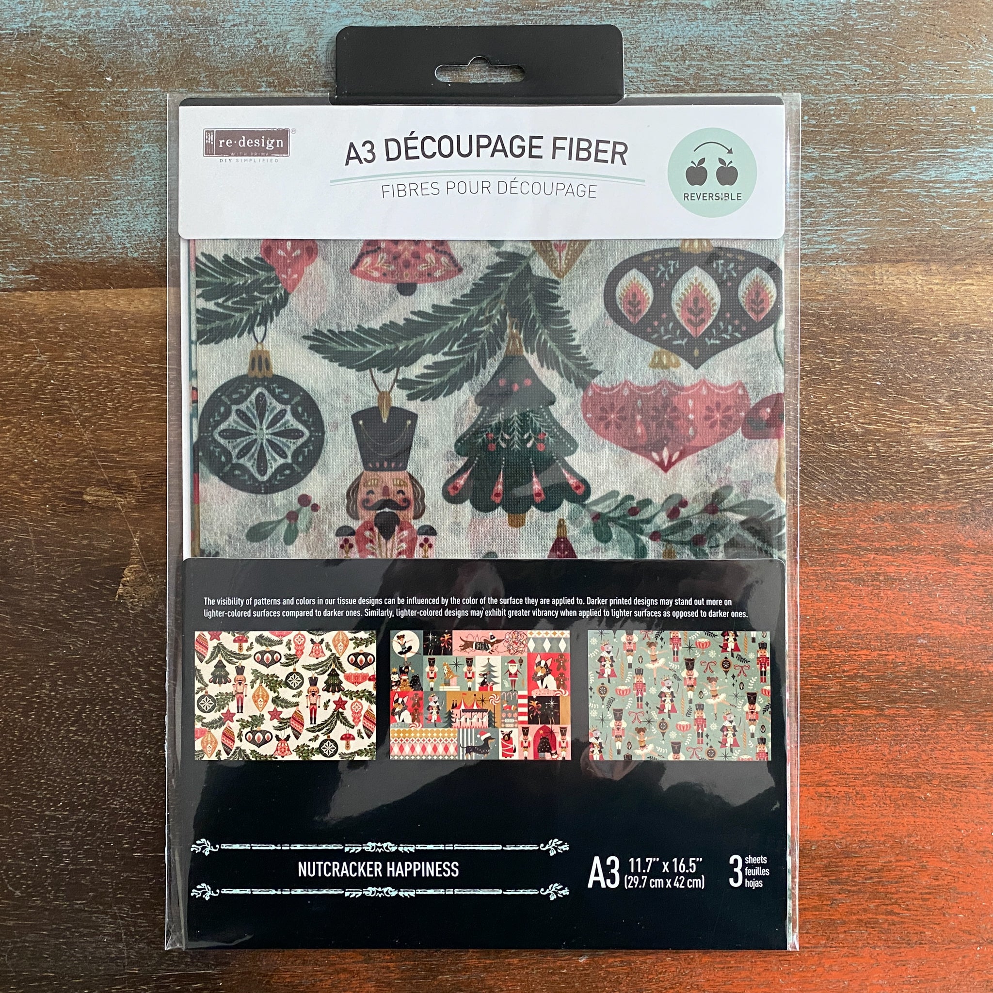 A package of ReDesign with Prima's Nutcracker Happiness fiber paper is against a dark wood background.