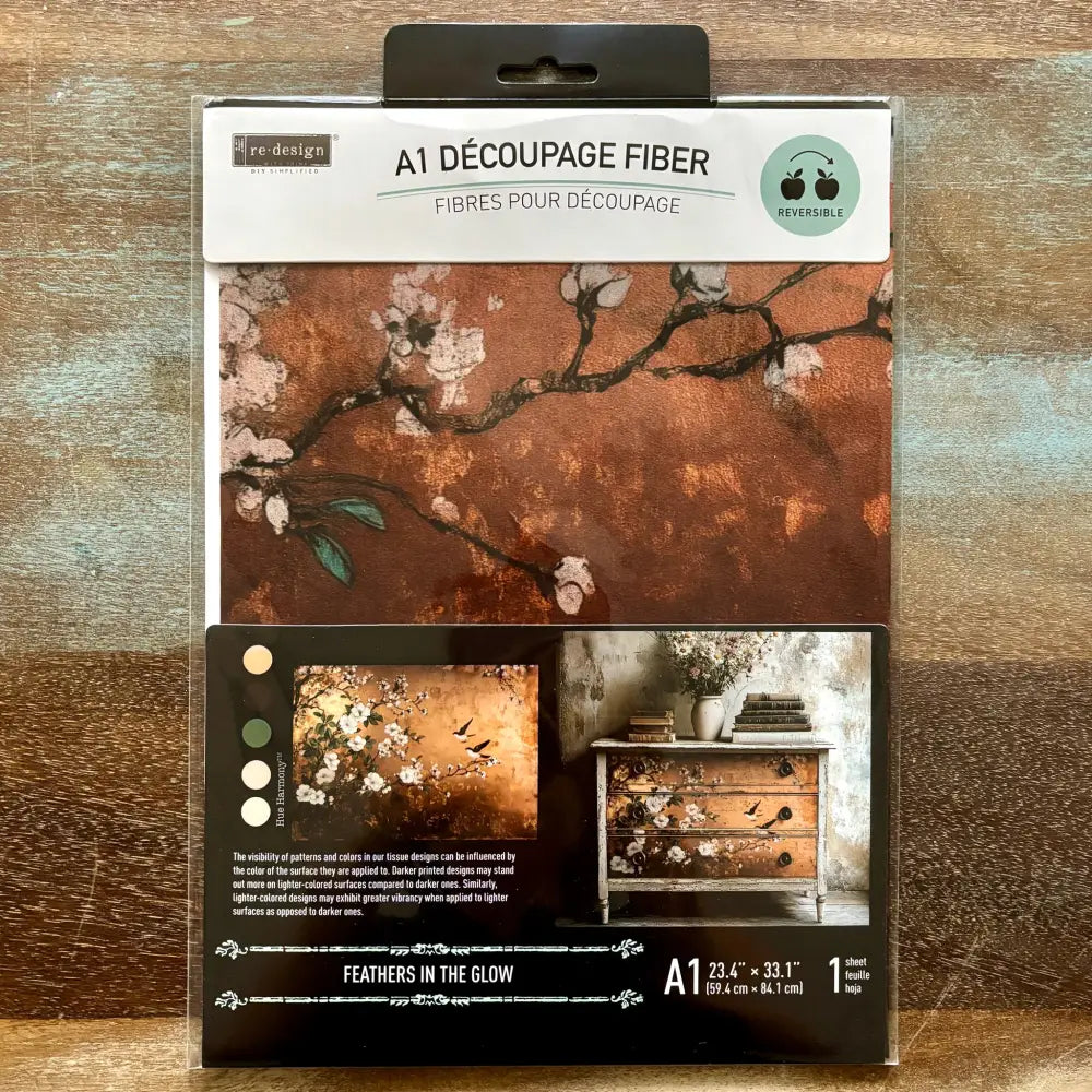 A package of ReDesign with Prima's Feathers in the Glow A1 fiber paper is against a wood background.