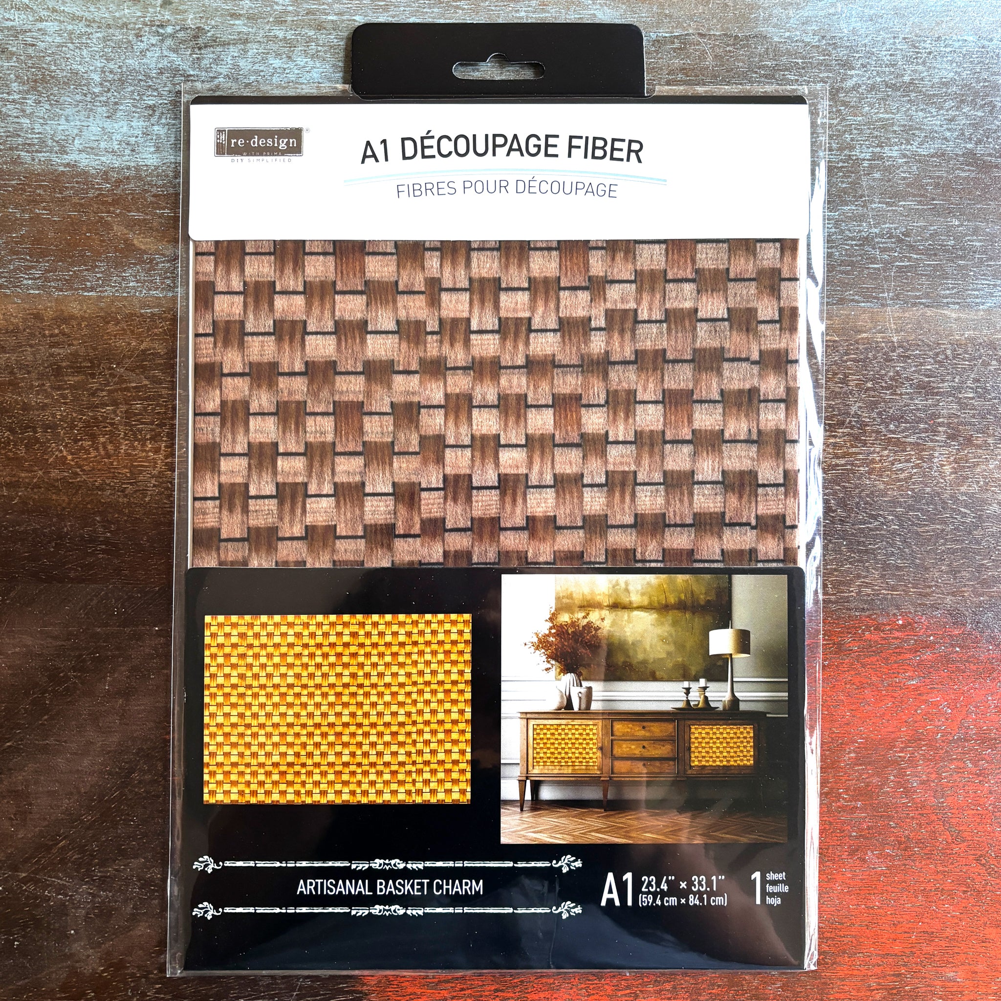 A package of ReDesign with Prima's Artisanal Basket Charm fiber paper is against a dark wood background.