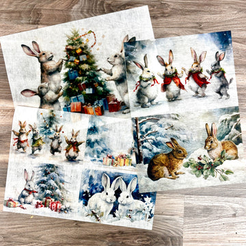 Three sheets of A3 fiber papers featuring scenes of bunnies in winter wonderlands are against a wood background.