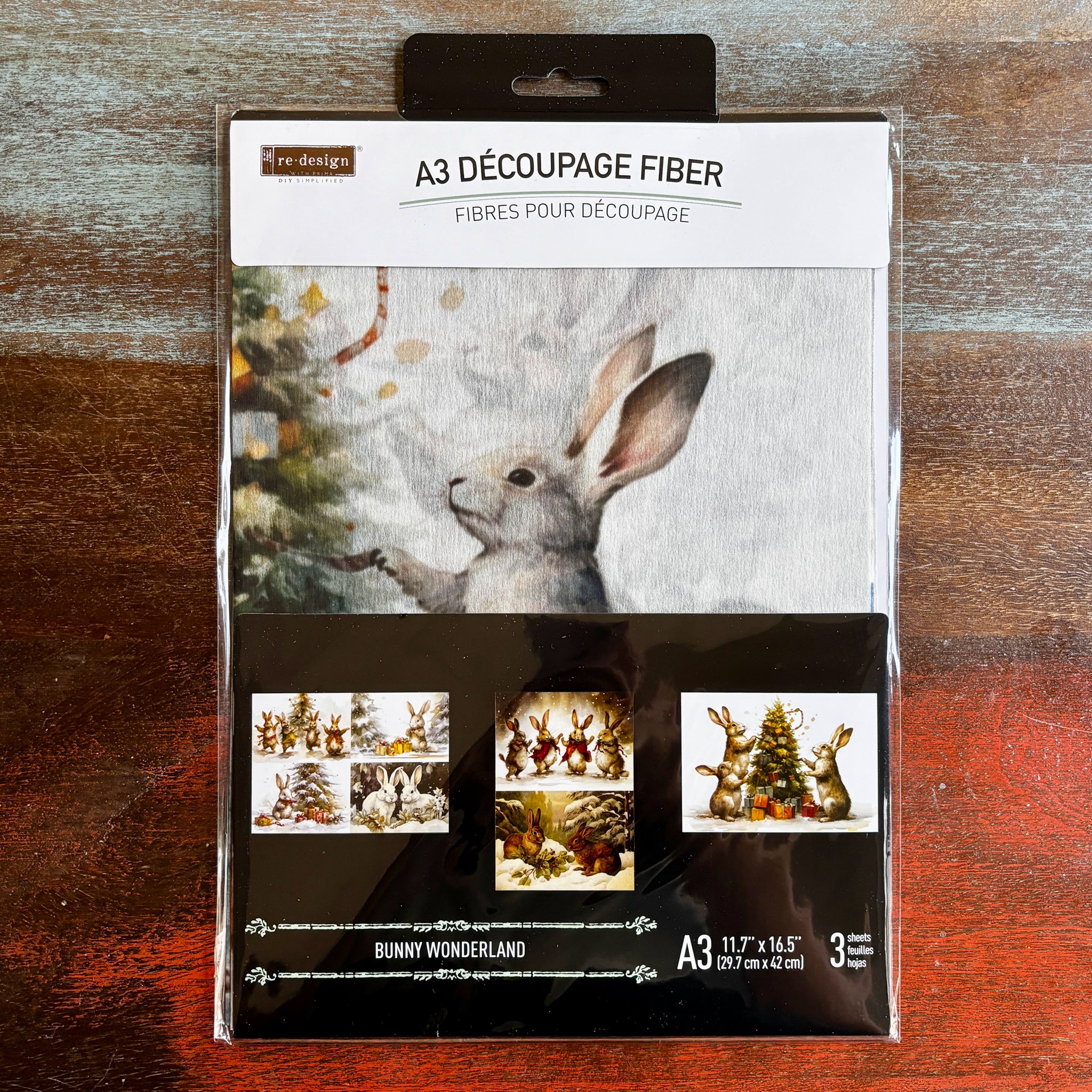 A package of ReDesign with Prima's Bunny Wonderland A3 fiber paper 3 pack is against a dark wood background.