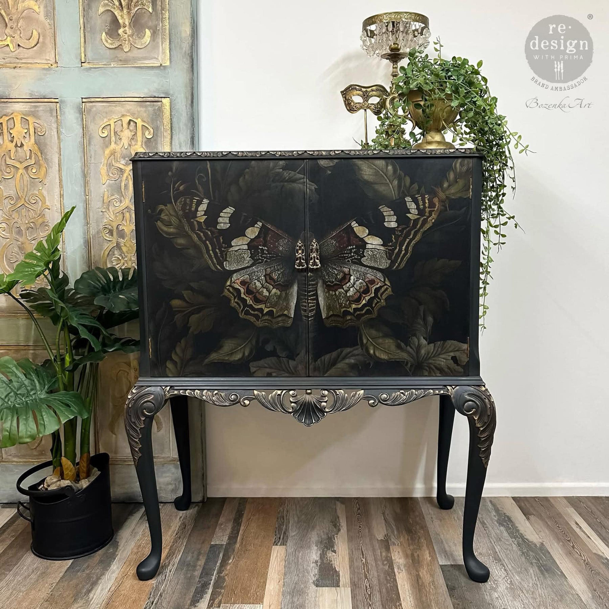 A vintage small buffet table is painted black with gold accents and features ReDesign with Prima's Butterfly Conservatory Tales fiber paper on its 2 doors.