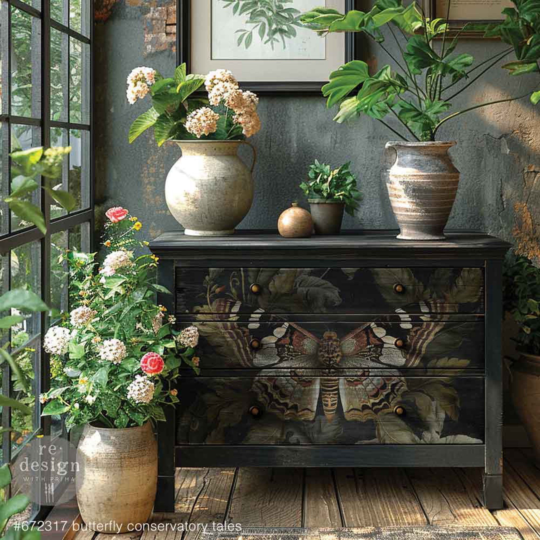 A 3-drawer dresser in a sunlit room with plants is painted black and features ReDesign with Prima's Butterfly Conservatory Tales A1 fiber paper on the drawers.