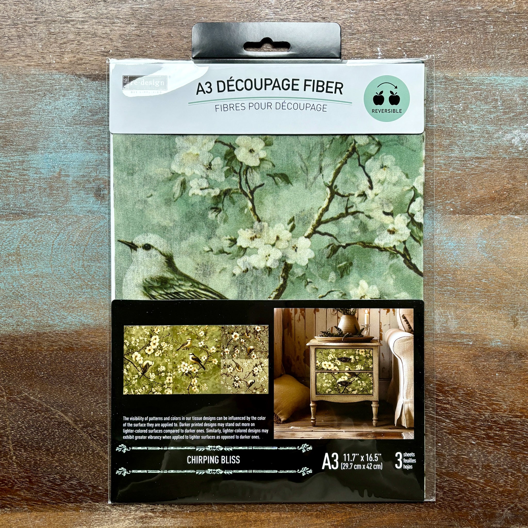 A package of ReDesign with Prima's Chirping Bliss A3 fiber paper 3 pack is against a wood background.