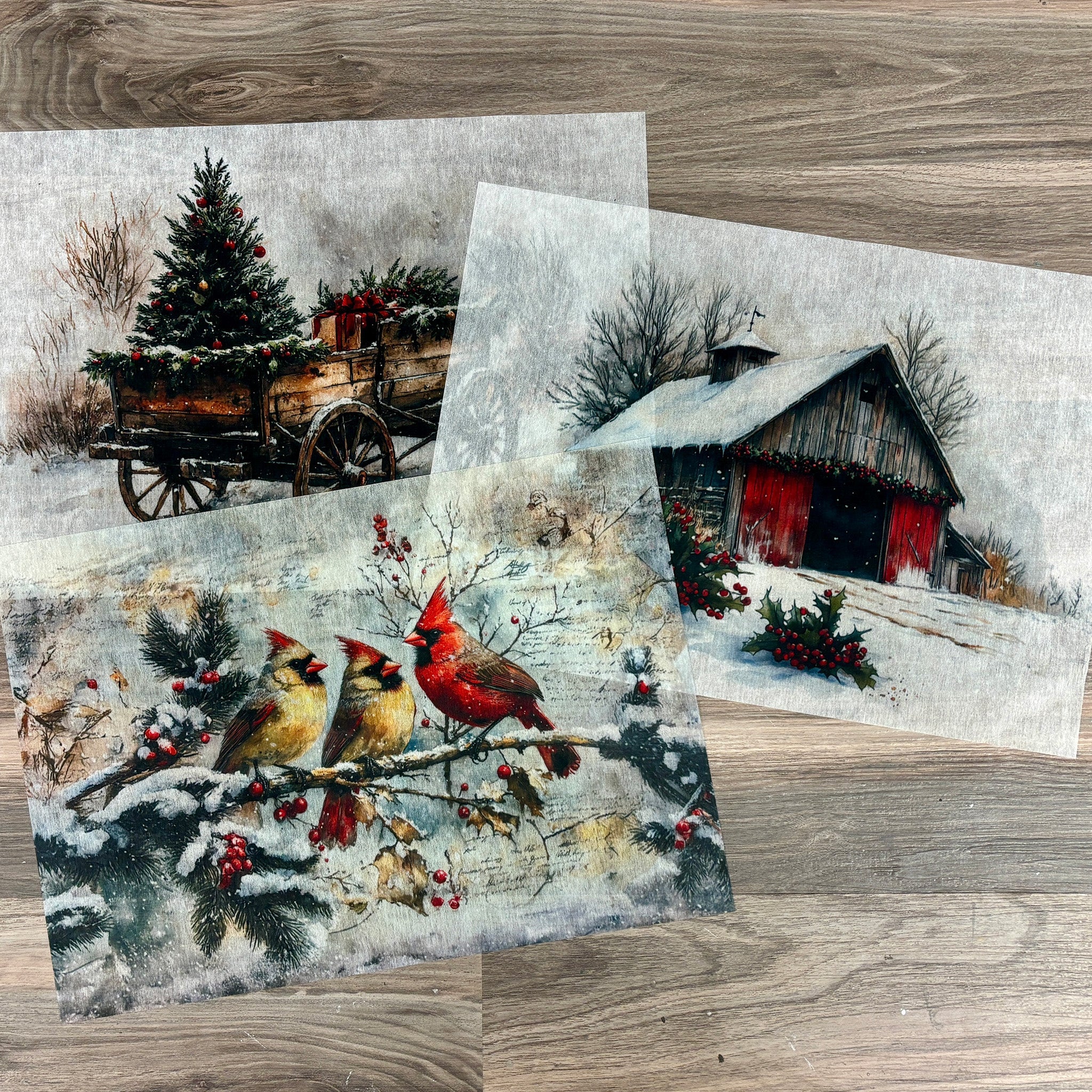 Three sheets of A3 fiber paper each with their own designs featuring a wagon hauling a Christmas tree and gifts, vibrant cardinals perched on a frosty branch, and a cozy barn nestled in a winter wonderland.