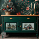 A small buffet table with a natural wood top is painted deep green and features 2 designs from ReDesign with Prima's Christmas in the Countryside A3 fiber papers on its 2 doors below 2 drawers.