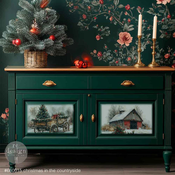 A small buffet table with a natural wood top is painted deep green and features 2 designs from ReDesign with Prima's Christmas in the Countryside A3 fiber papers on its 2 doors below 2 drawers.