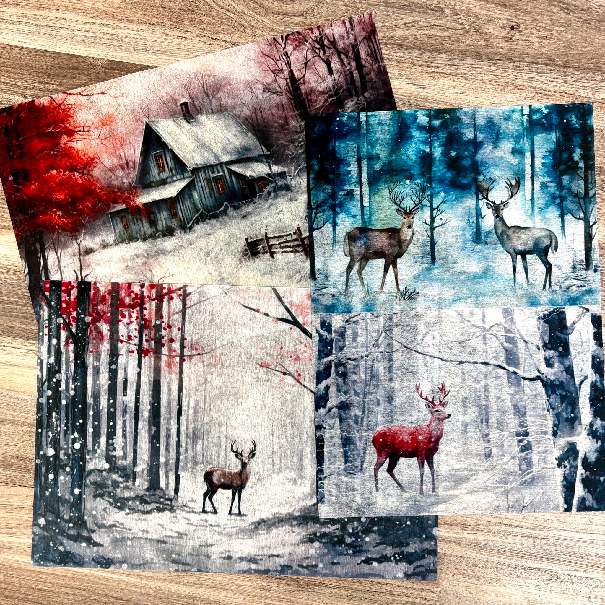 Three sheets of A3 fiber papers featuring a cabin, and deer in snow covered forests are against a wood background.