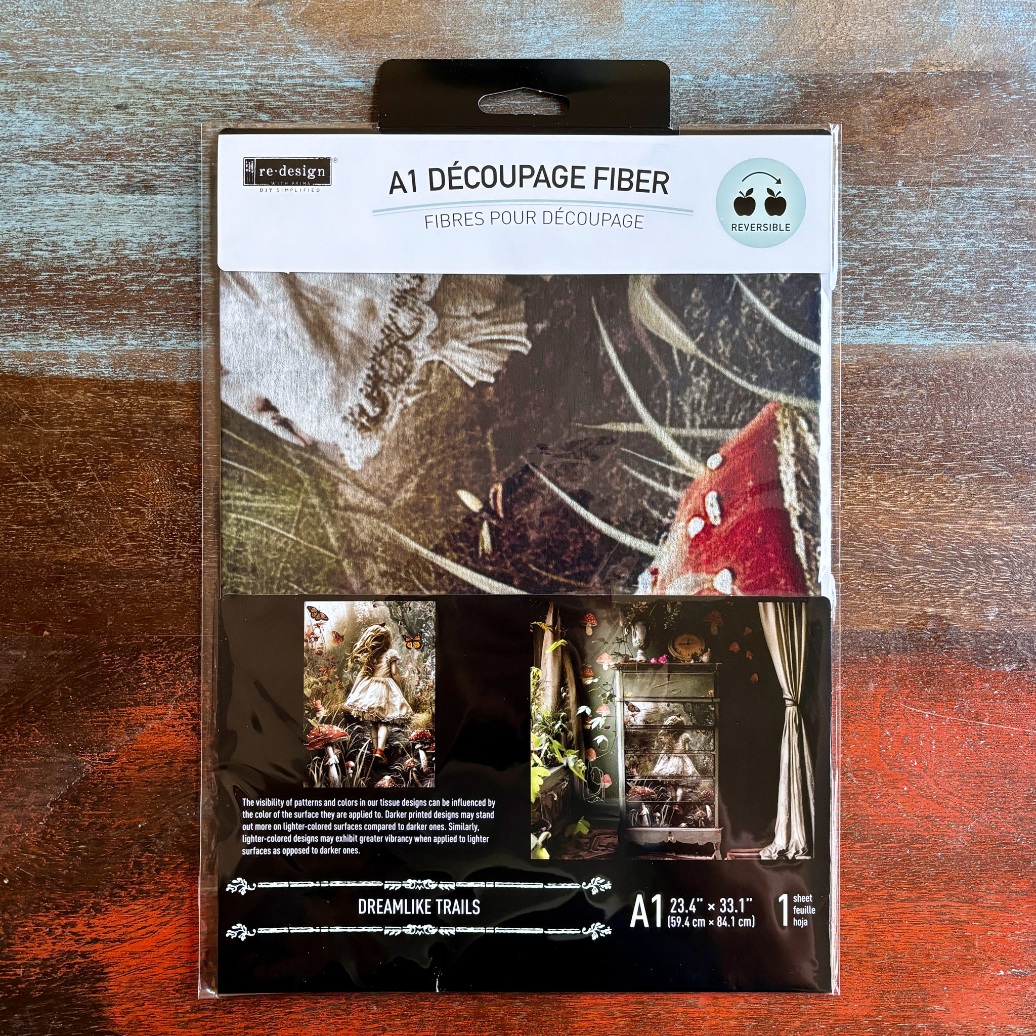 A package of ReDesign with Prima's Dreamlike Trails A1 fiber paper is against a dark wood background.