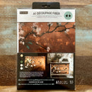 A package of ReDesign with Prima's Feathers in the Glow A1 fiber paper is against a wood background.